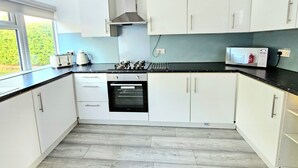 A modern kitchen with white cabinets, a black countertop, a built-in oven, a microwave, and a window providing a view of greenery outside. - Spacious Haven with Free Parking (Glasgow)