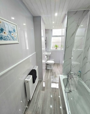 A modern bathroom with a marble floor, a bathtub, a toilet, and a sink. - Spacious Haven with Free Parking (Glasgow)