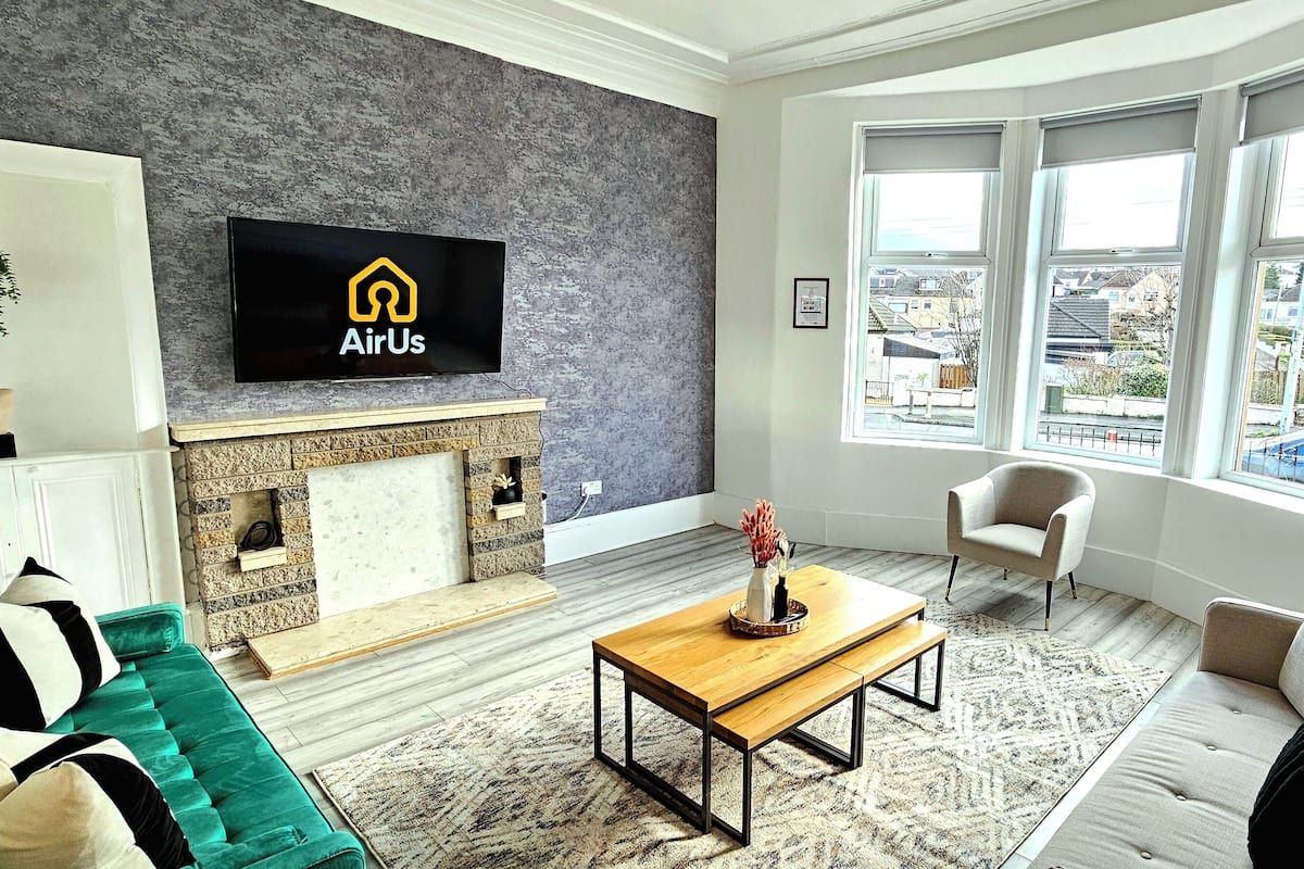 A modern living room with a fireplace, a sofa, a coffee table, and a television displaying the AirUs logo.