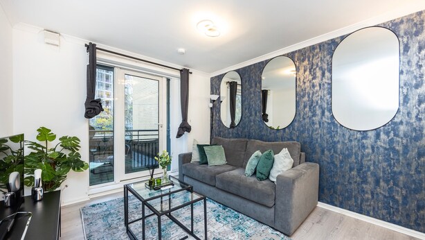 A modern living room with a grey sofa, a glass door leading to a balcony, and a blue textured wall. - London Oasis Apartment Escape (London)