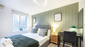 A bedroom with a bed, bedside table, chair, and a window with a view of buildings. - London Oasis Apartment Escape (London)