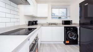 A modern kitchen with white cabinetry, a built-in microwave, a black washing machine, and a glass-fronted stove. - London Oasis Apartment Escape (London)