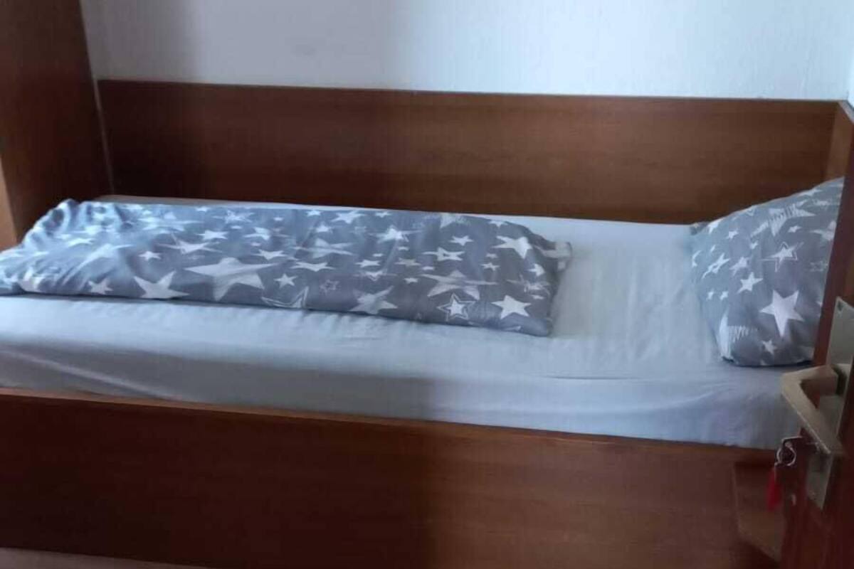 Un lit simple avec une couverture et un oreiller à motifs d’étoiles grises et blanches, une tête de lit en bois et un plancher en bois.
