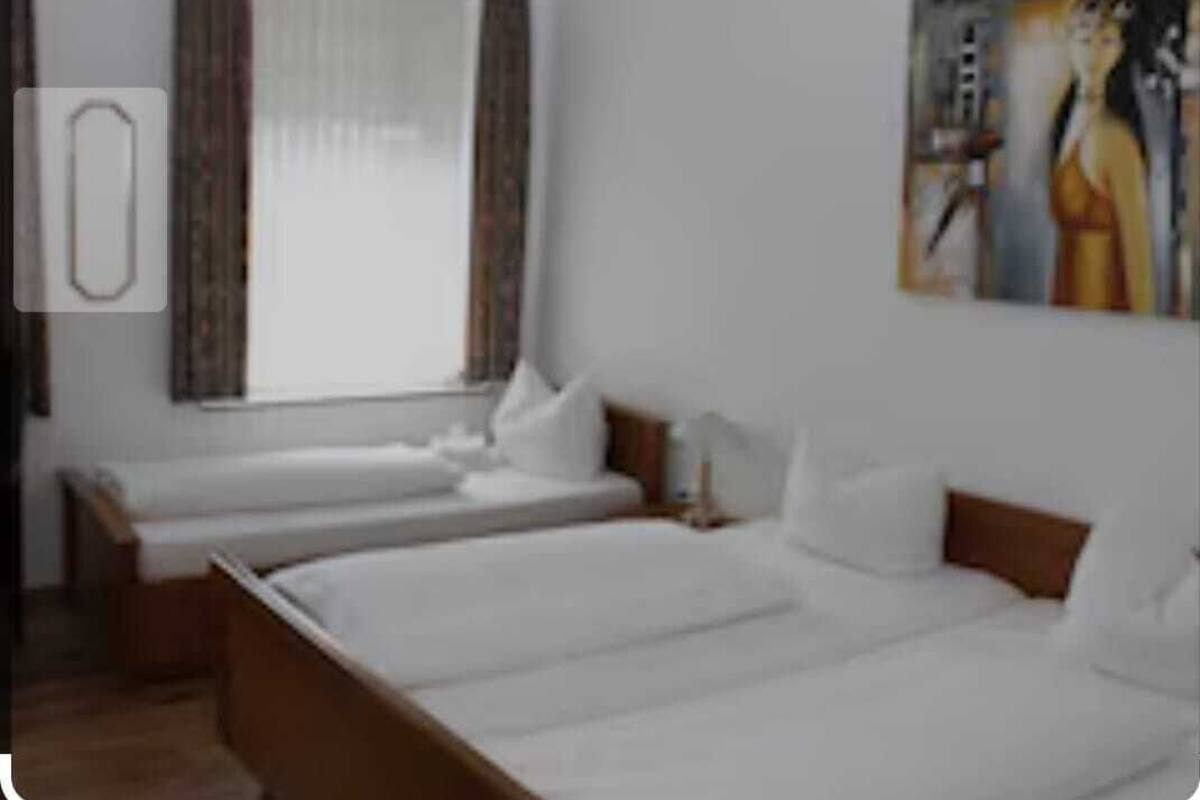 Une chambre d’hôtel avec deux lits simples, une grande fenêtre avec des rideaux et un tableau au mur.