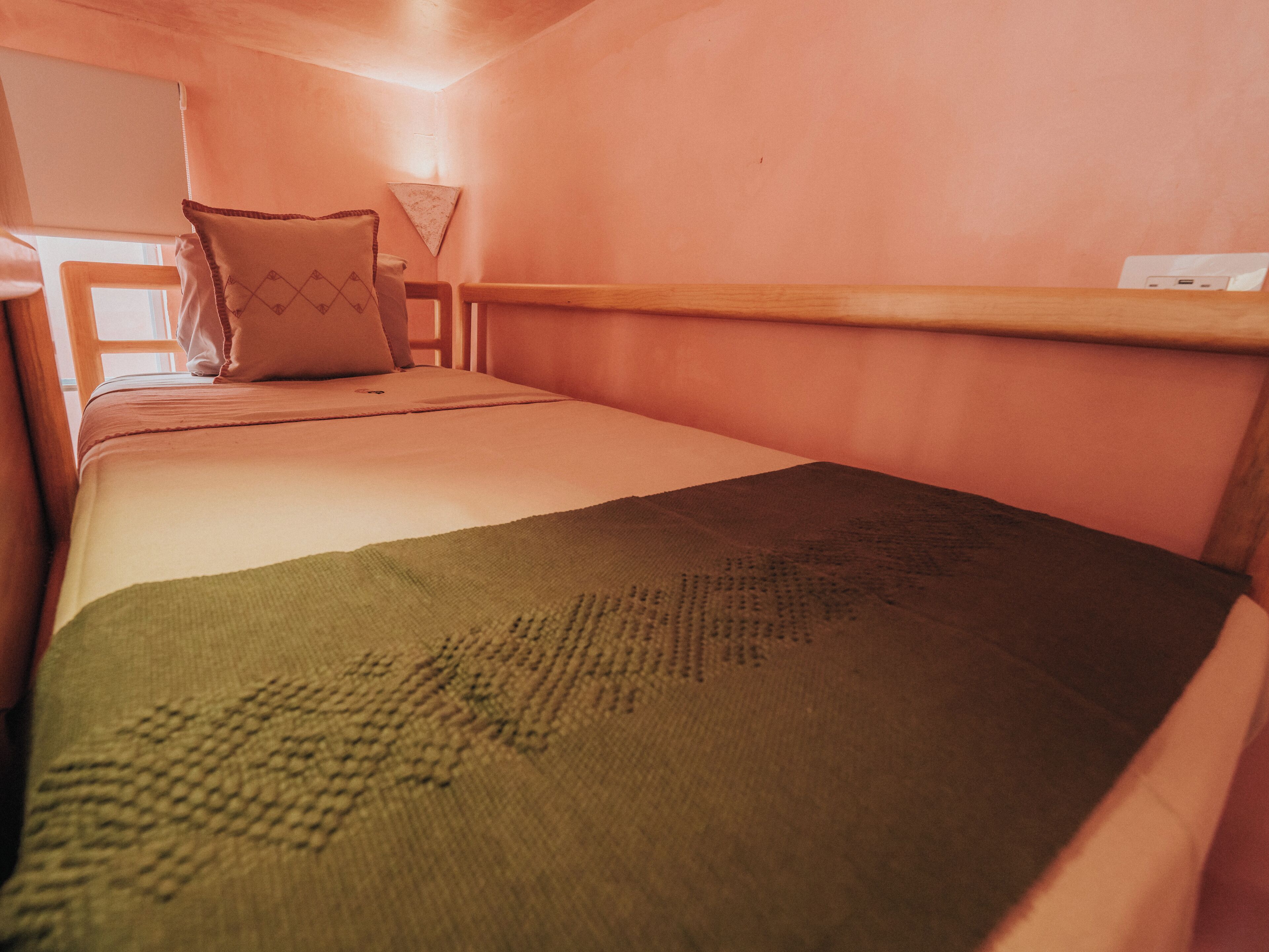 A single bed with a green blanket, a wooden headboard, and a bedside table with a lamp.