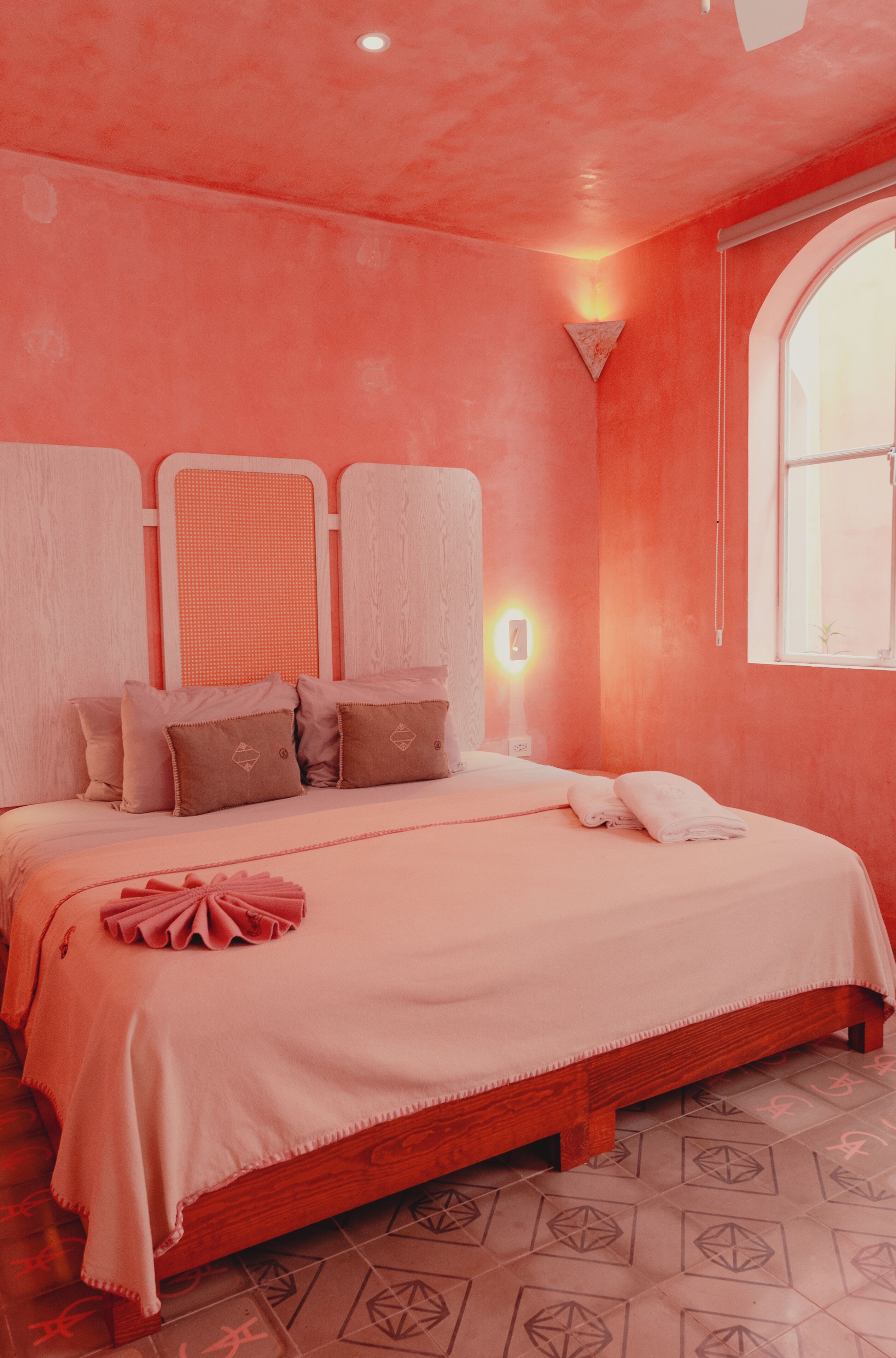 Un dormitorio con cama, almohadas, una mesita de noche y una ventana.