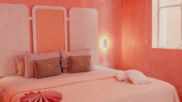 Un dormitorio con cama, almohadas, una mesita de noche y una ventana.