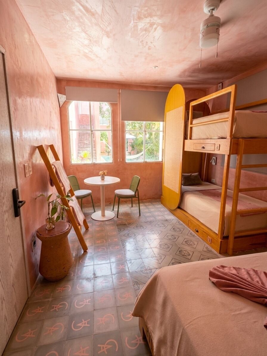 A room with bunk beds, a small table, chairs, a window, and a ceiling fan.