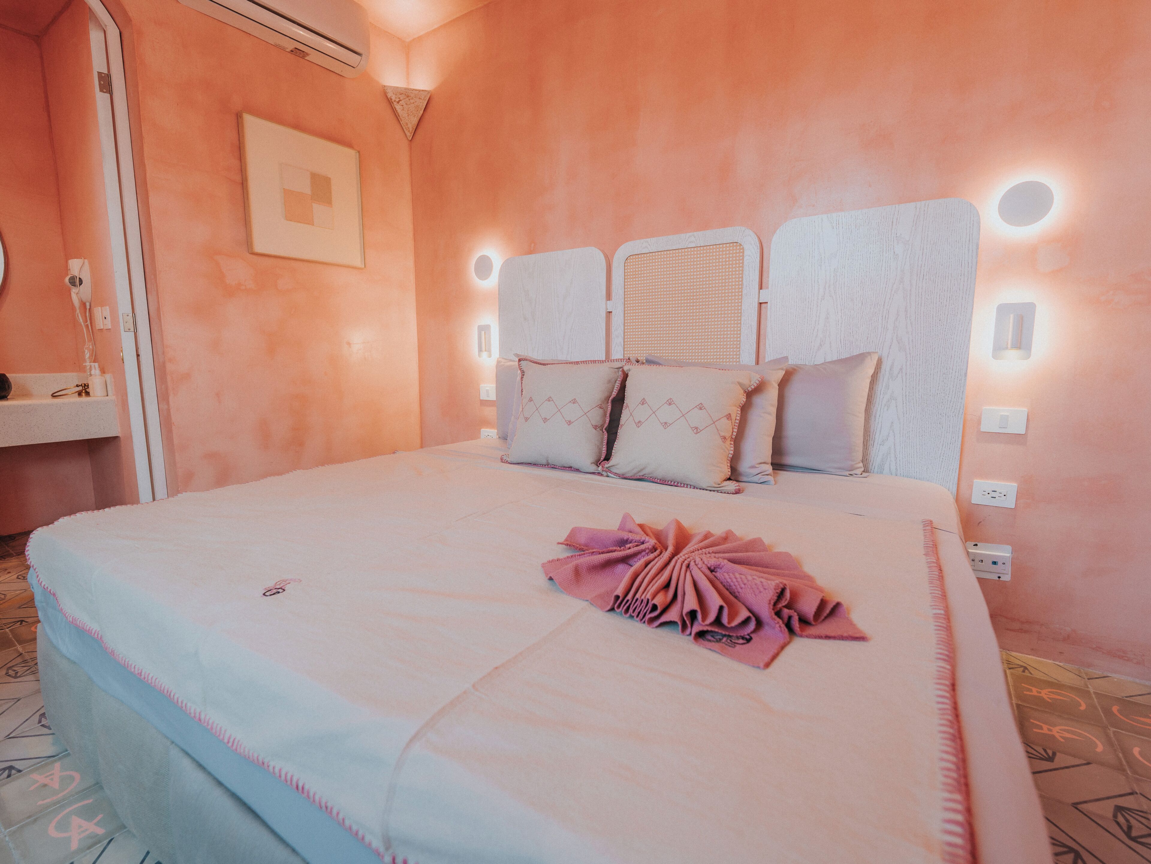 A bedroom with a bed, bedside lamps, a wall-mounted air conditioner, and a framed picture on the wall.