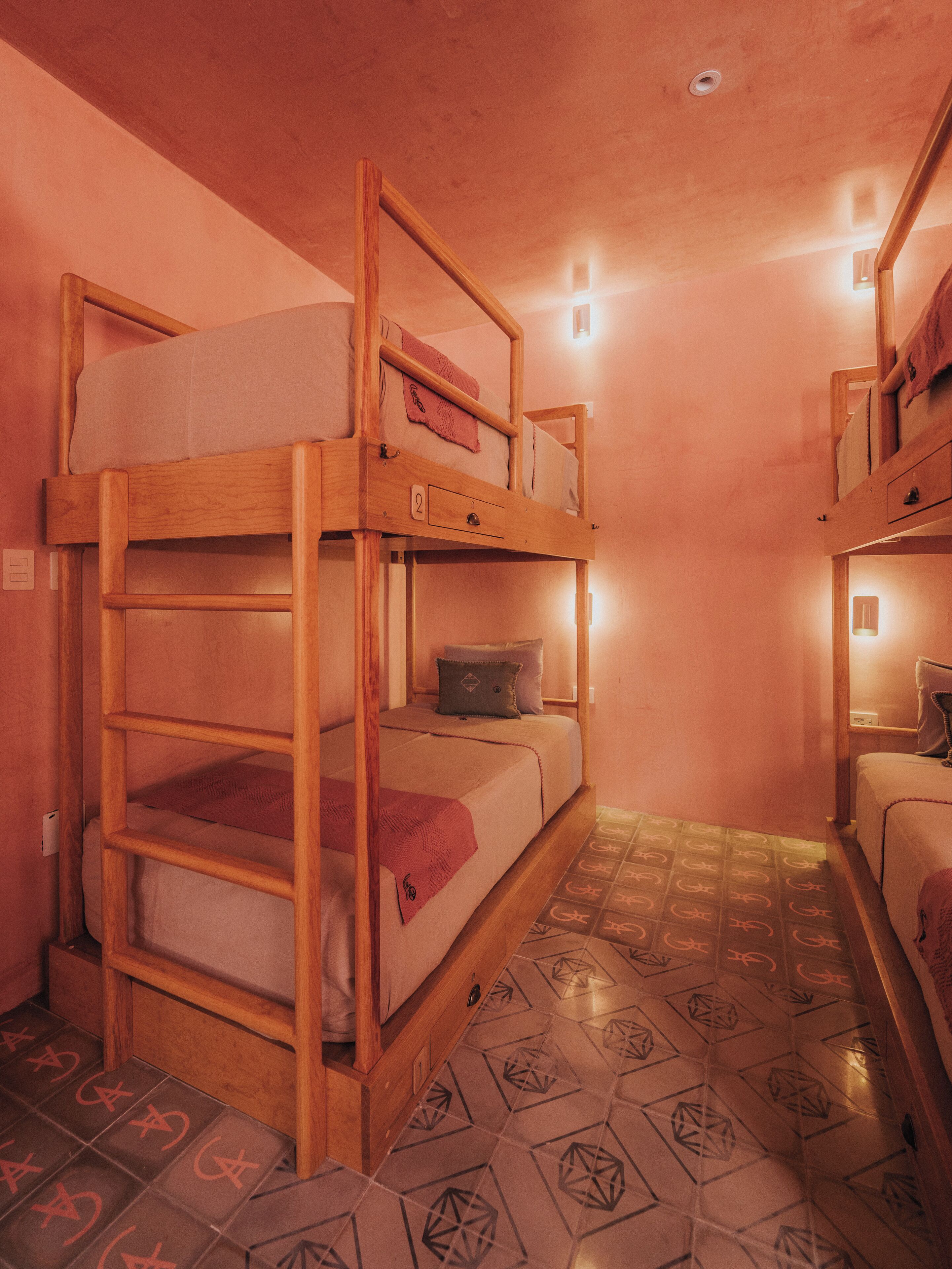 A dormitory room with bunk beds, a tiled floor, and a wall socket.