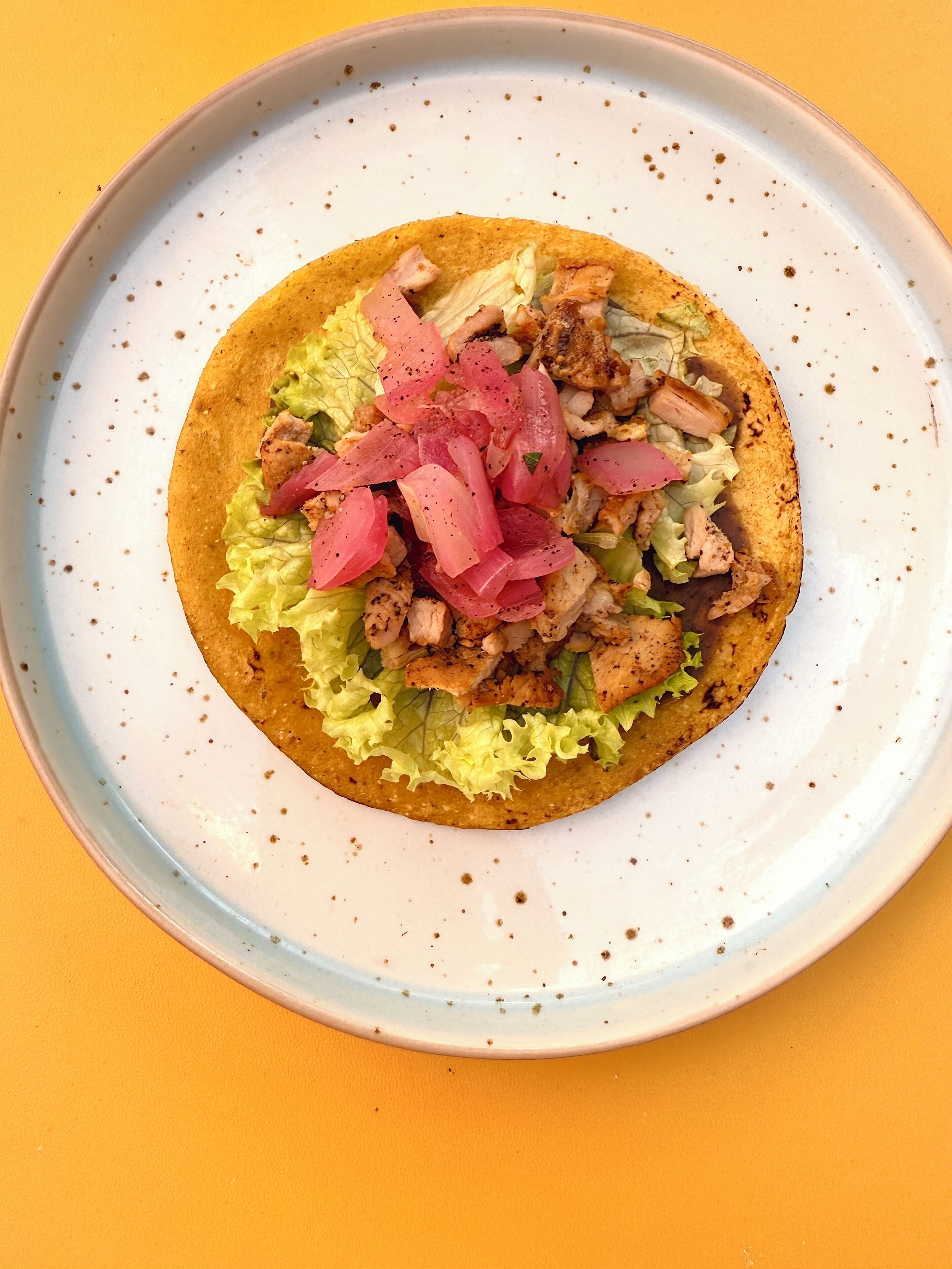 A taco with lettuce and pink pickled onions on a plate.