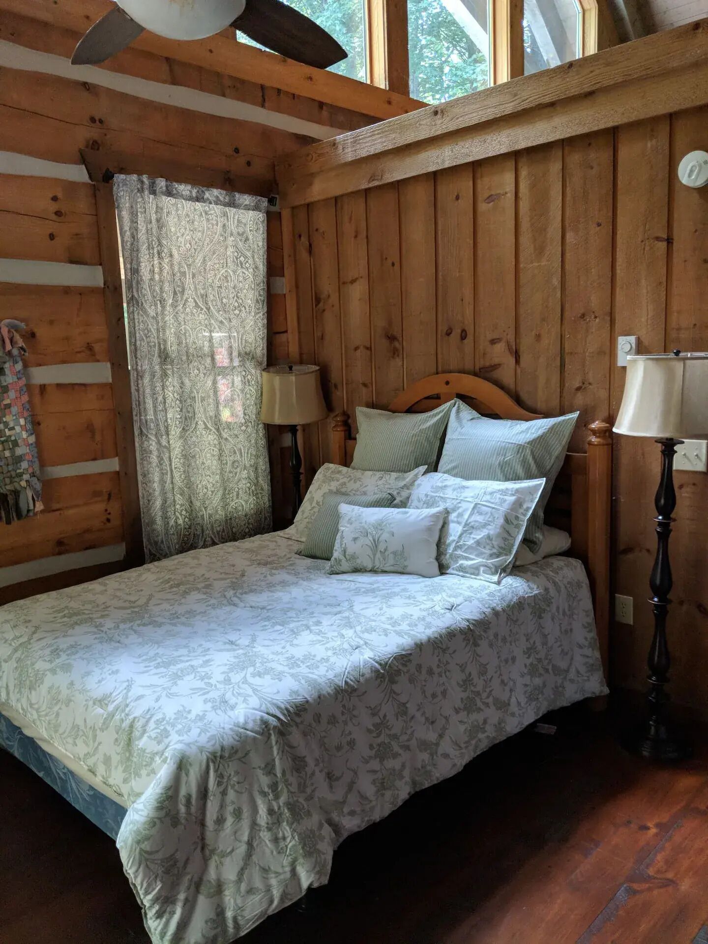 Ein Schlafzimmer in einer Holzhütte mit einem Bett, zwei Nachttischlampen und einem Fenster mit Vorhängen.