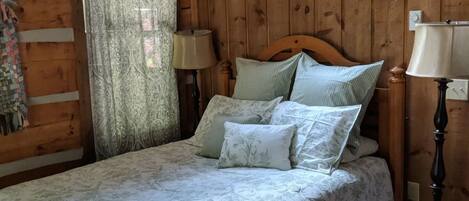 Ein Schlafzimmer in einer Holzhütte mit einem Bett, zwei Nachttischlampen und einem Fenster mit Vorhängen.