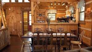 A wooden cabin interior with a dining area, kitchen, and a bar.