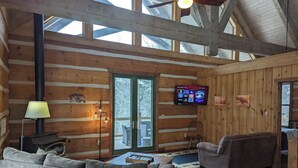 A log cabin interior with a fireplace, sofa, television, and a dining area.