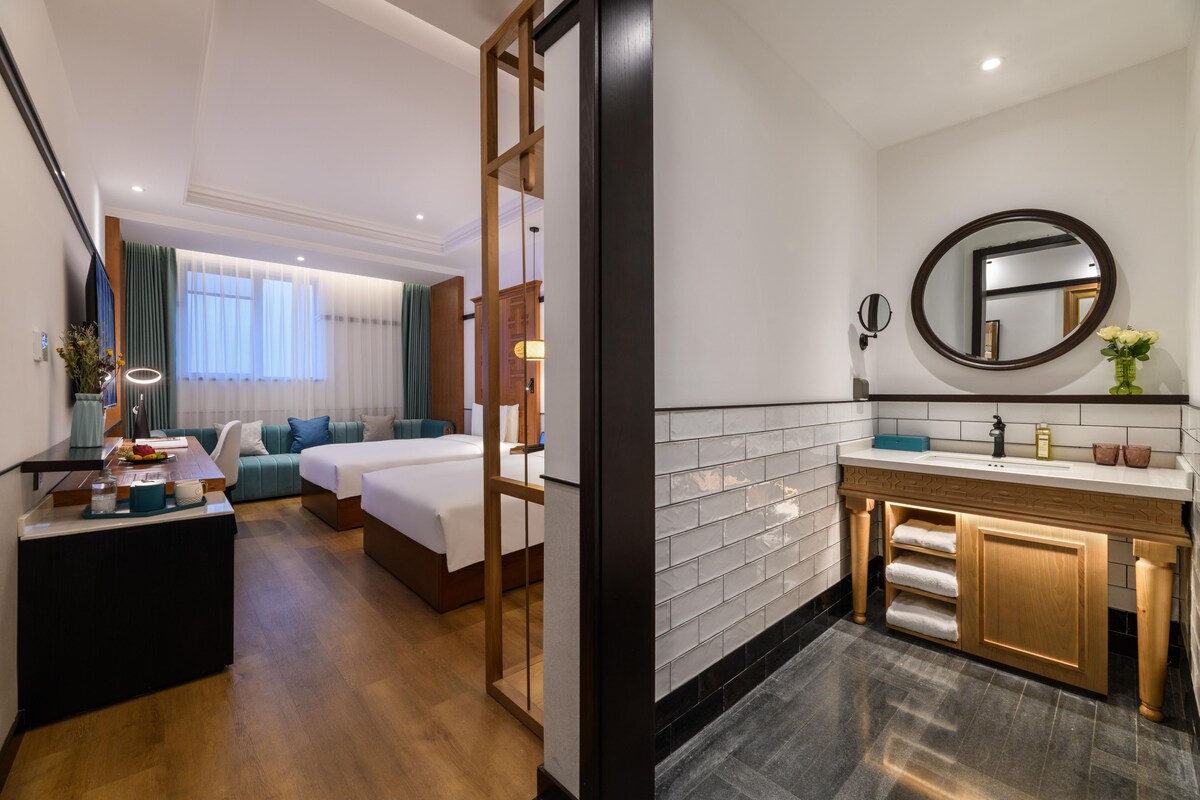 A hotel room with a bed, a desk, a sofa, a bathroom with a sink and mirror.