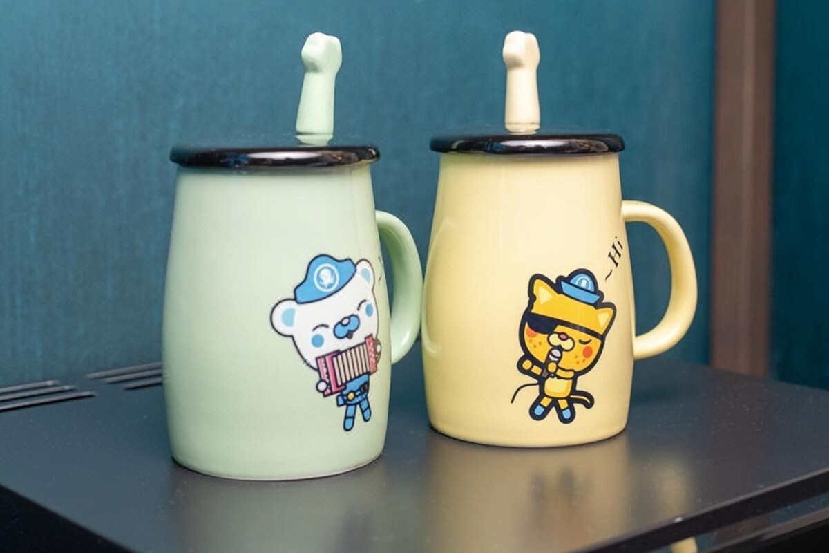 Two ceramic mugs with cartoon characters on them, placed on a shelf.