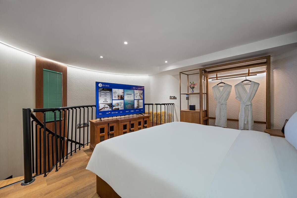 A hotel room with a bed, a TV, a wooden cabinet, a robe rack, and a staircase.