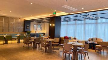 A modern hotel lobby with a reception desk, seating area, and large windows.