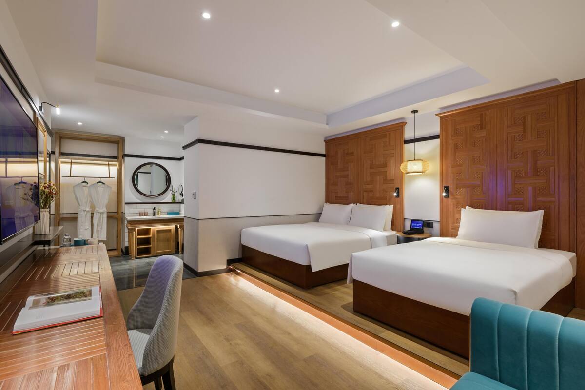 A hotel room with two beds, a desk with a chair, a vanity with a mirror, and a television.