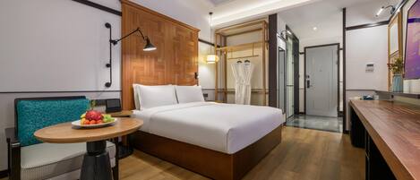 A hotel room with a bed, a small table with fruit, a chair, a wooden cabinet, and a mirror.