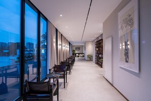 Corredor moderno de hotel com uma mesa comprida e cadeiras, uma estante e obras de arte nas paredes.