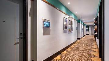 A hotel hallway with a patterned carpet, framed pictures on the walls, and a door with a digital display.