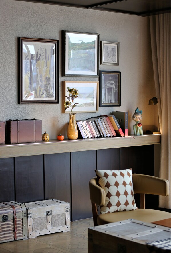 Quarto com estante de livros, quadros, um vaso com flores e uma figurinha decorativa.