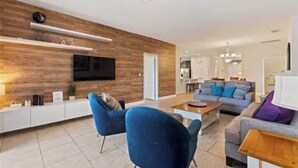 Un soggiorno moderno con una parete in legno decorativa, una TV a schermo piatto, poltrone blu e un divano grigio.