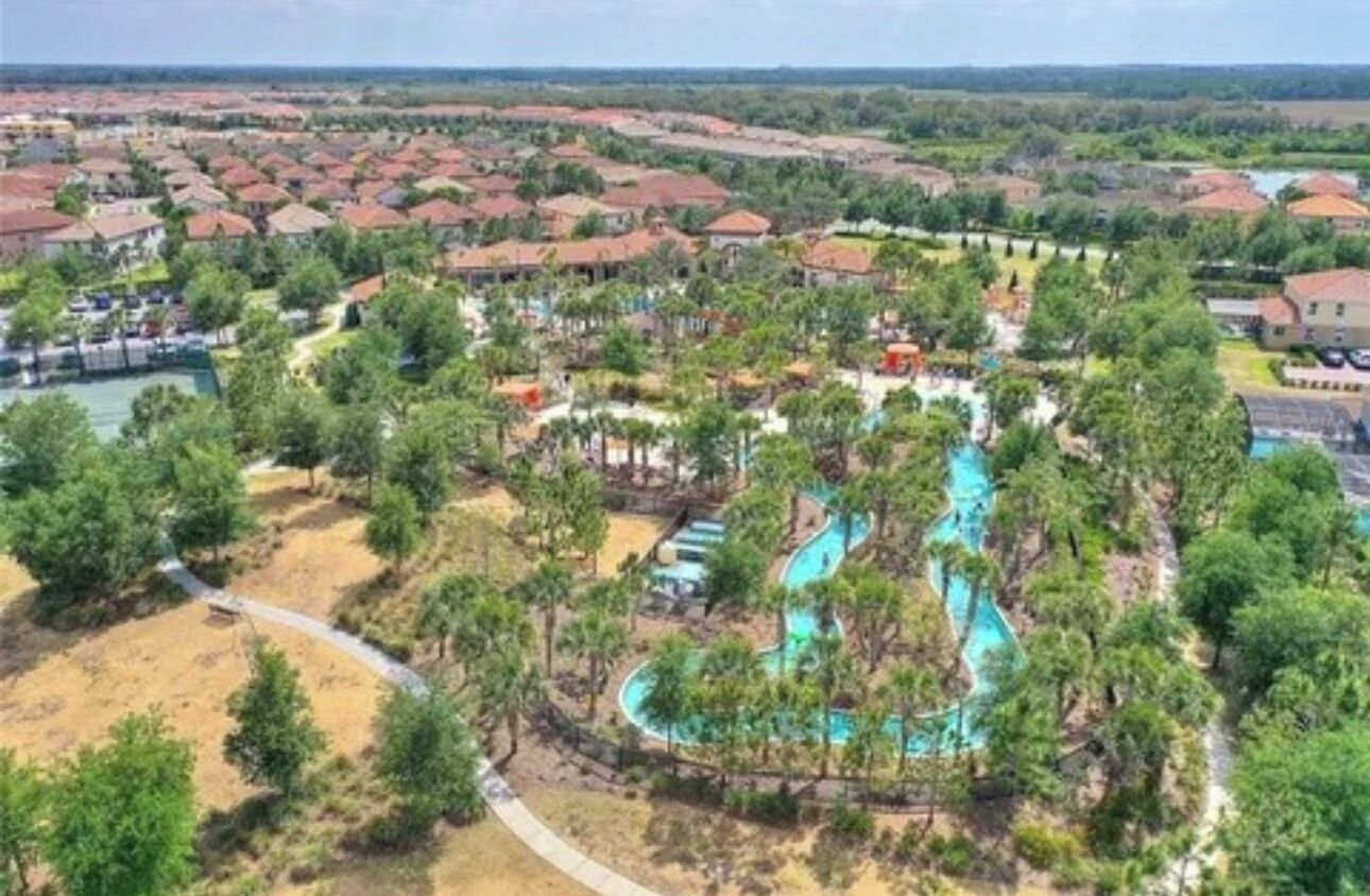 A resort with a large pool area, surrounded by lush greenery and residential buildings.