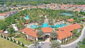Un quartiere residenziale con una piscina centrale circondata da case con tetti in tegole rosse e palme.