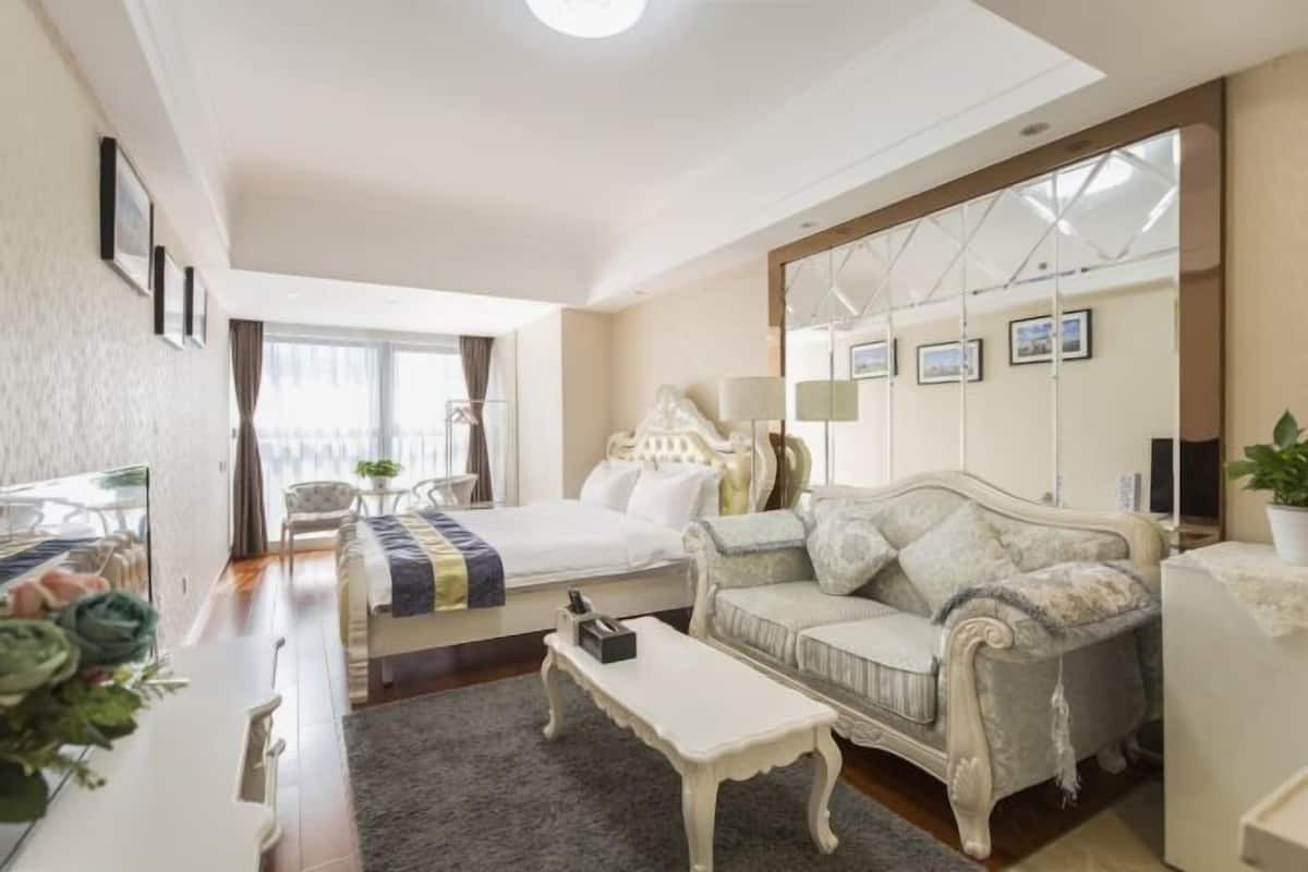 A hotel room with a bed, a sofa, a dining table, and a large mirror.