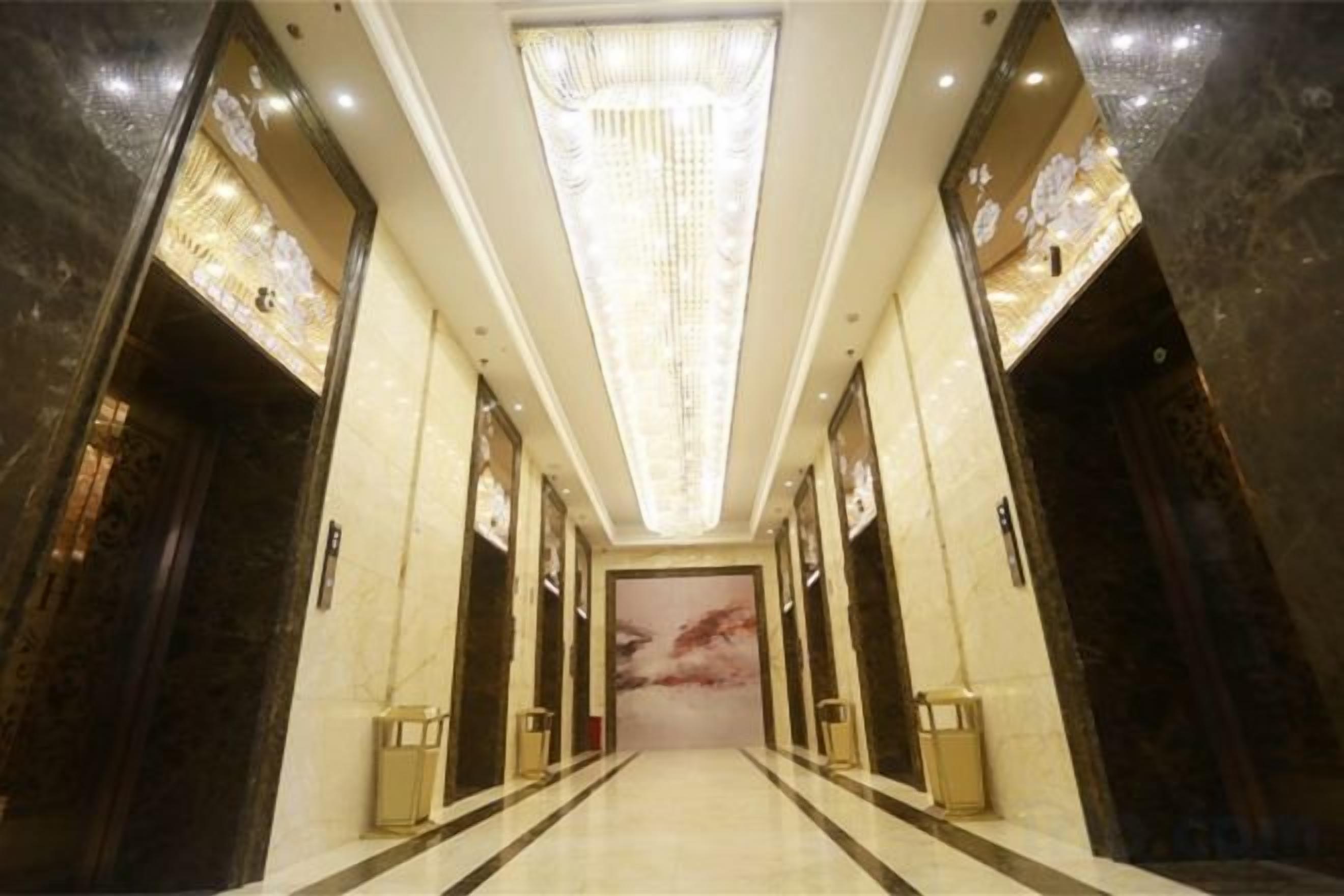 Corredor de hotel com lustre, paredes de mármore e um grande mural.