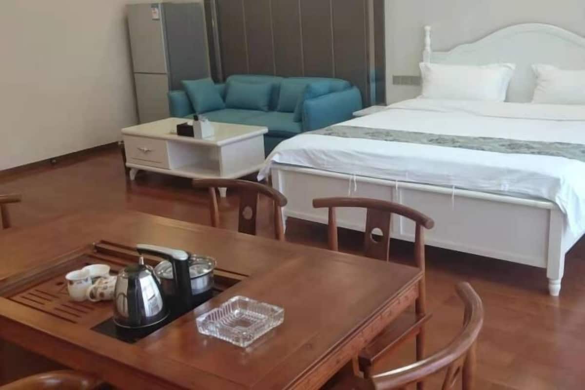 A hotel room with a bed, a blue sofa, a dining table with chairs, and a small white table.