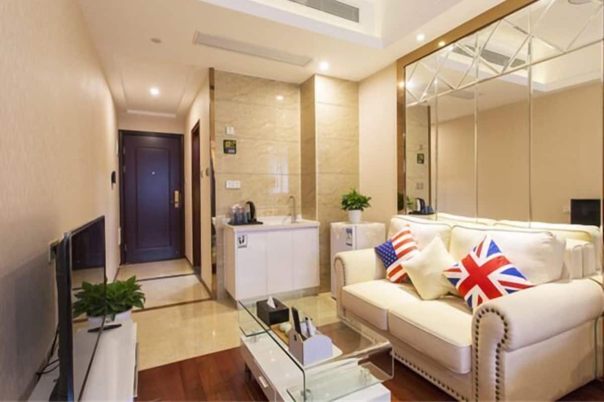 A modern living room with a sofa, a coffee table, a TV, and a kitchen area with a sink and cabinets.