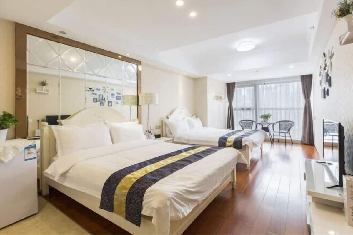 A hotel room with two beds, a desk, a chair, a TV, and a large window.