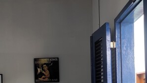 Une pièce avec une table et des chaises bleu clair, un panneau noir accroché au mur et une fenêtre avec des volets bleus.