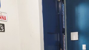 Un couloir avec une porte bleue, une étagère en bois et un interrupteur fixé au mur.