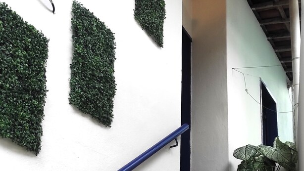 Un escalier aux marches de couleur beige menant à un palier, avec des murs blancs et des décorations en feuilles artificielles vertes.