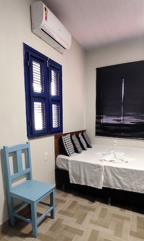 A room with a bed, a blue chair, a window with blinds, and an air conditioning unit. - Casa das Flores (Jijoca de Jericoacoara)