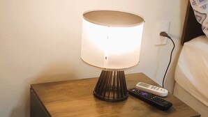 Une table de chevet avec une lampe, une télécommande et une prise électrique, le tout posé sur une table de nuit en bois.