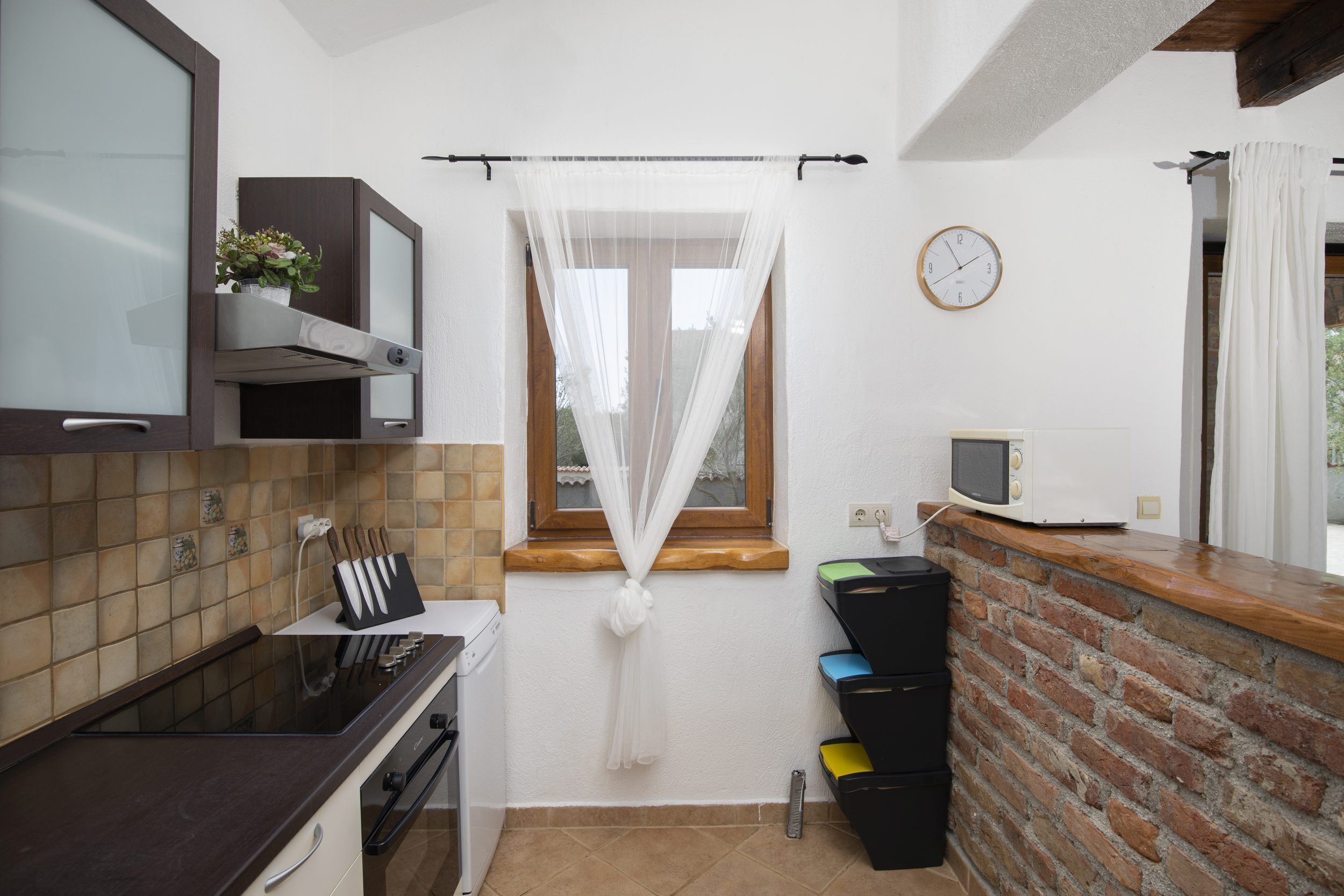Cocina compacta con microondas, estufa y una ventana pequeña con cortinas traslúcidas.