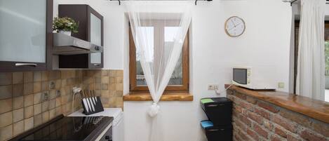 Cocina compacta con microondas, estufa y una ventana pequeña con cortinas traslúcidas.