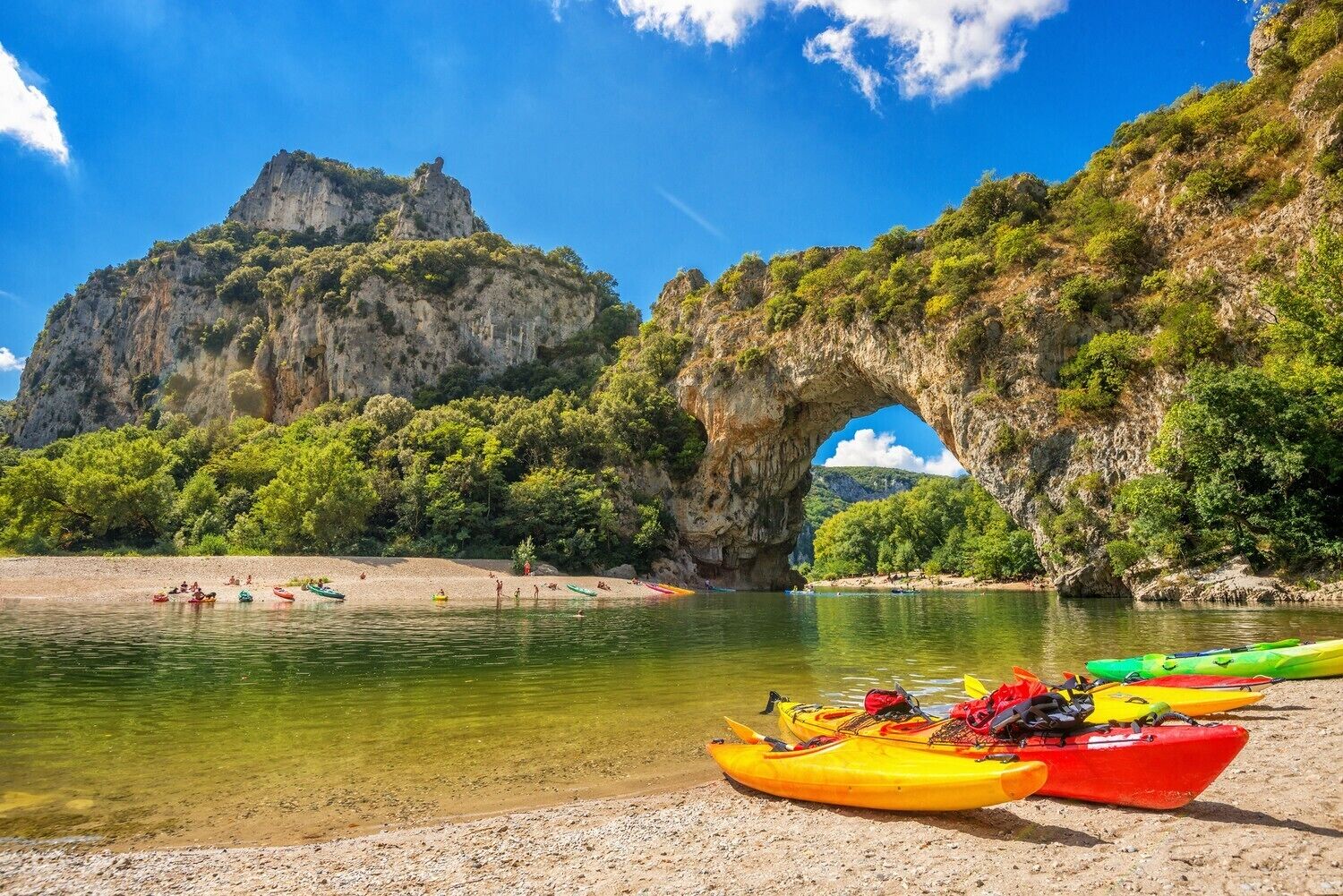 A beach with kayaks and a natural rock arch.
