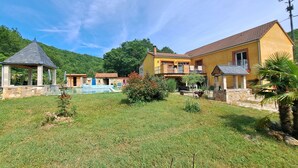 A yellow building with a tiled roof, a stone pool, and a gazebo.