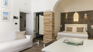 A hotel room with a white bed, a white sofa, a stone pillar, and a glass coffee table.