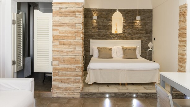 A bedroom with a stone accent wall, a bed with two pillows, and a white bedside table.