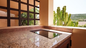 Une cuisine dotée d’un plan de travail en granit, d’une cuisinière encastrée et offrant une vue sur un cactus par la fenêtre.