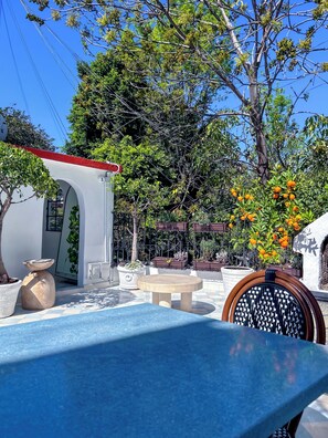 Relax in a serene outdoor space surrounded by lush greenery and trees, featuring a round table and a woven chair.