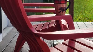 Una poltrona Adirondack rossa su un pontile di legno con una tazza di metallo con un disegno di un orso.
